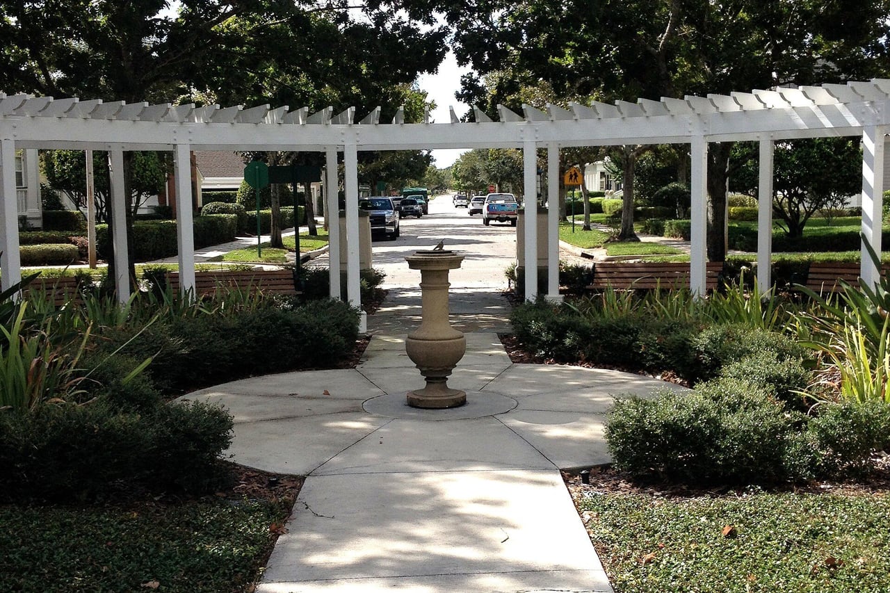 Pérgola branca sobre caminho de concreto num jardim entre as casas