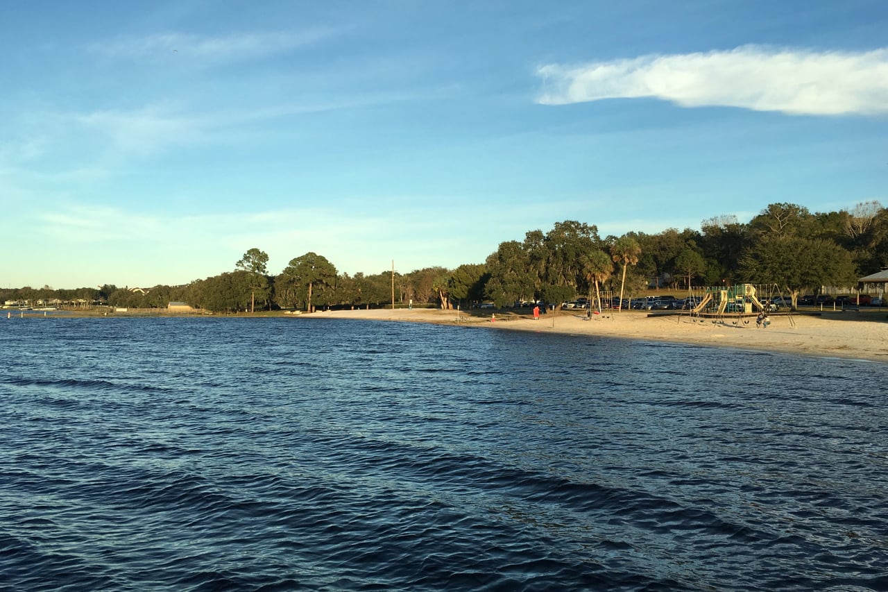 Praia com parquinho e árvores na margem do Lago Minneola, vista da água.