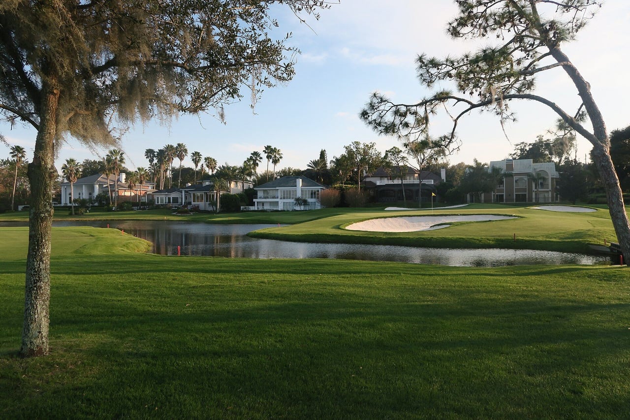Campo de golfe com lago e banco de areia e casas grandes ao fundo