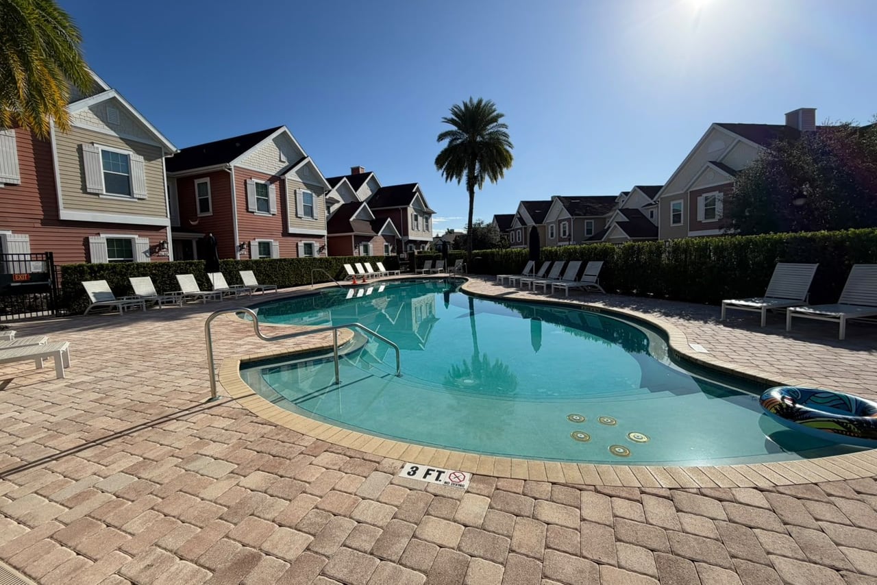 Piscina de condomínio com espreguiçadeiras e palmeira, cercada por townhouses