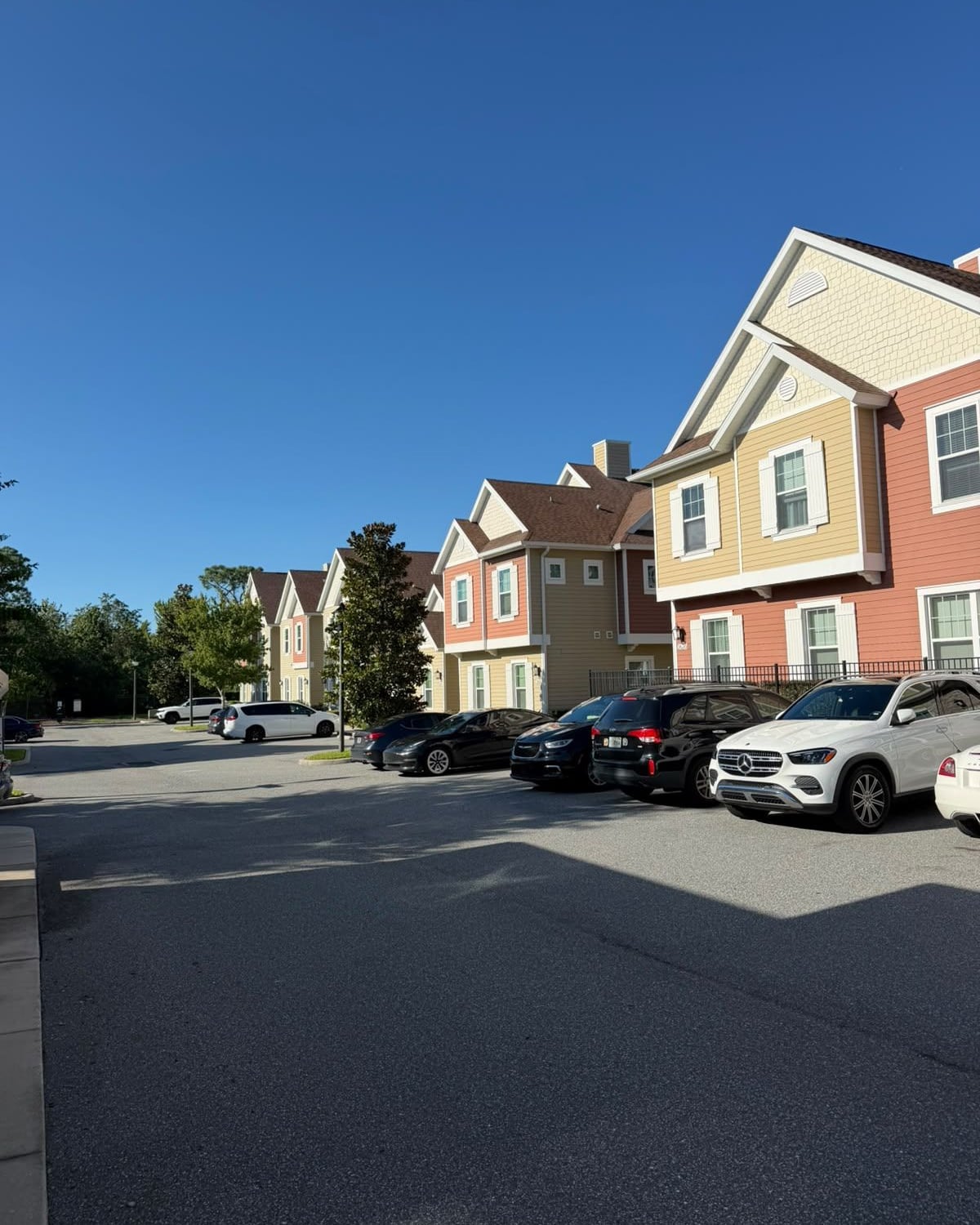 Townhouses de três andares em tons de terracota e bege, com carros estacionados à frente